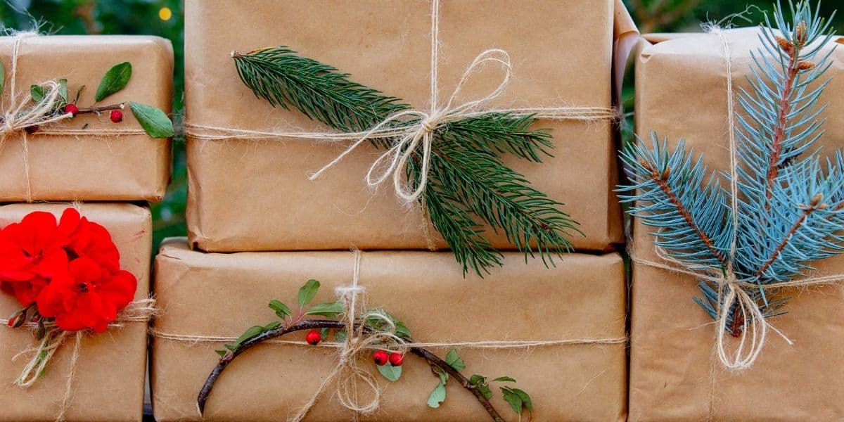 Five gifts wrapped in brown paper, tied with twine, and decorated with fresh Christmas greenery