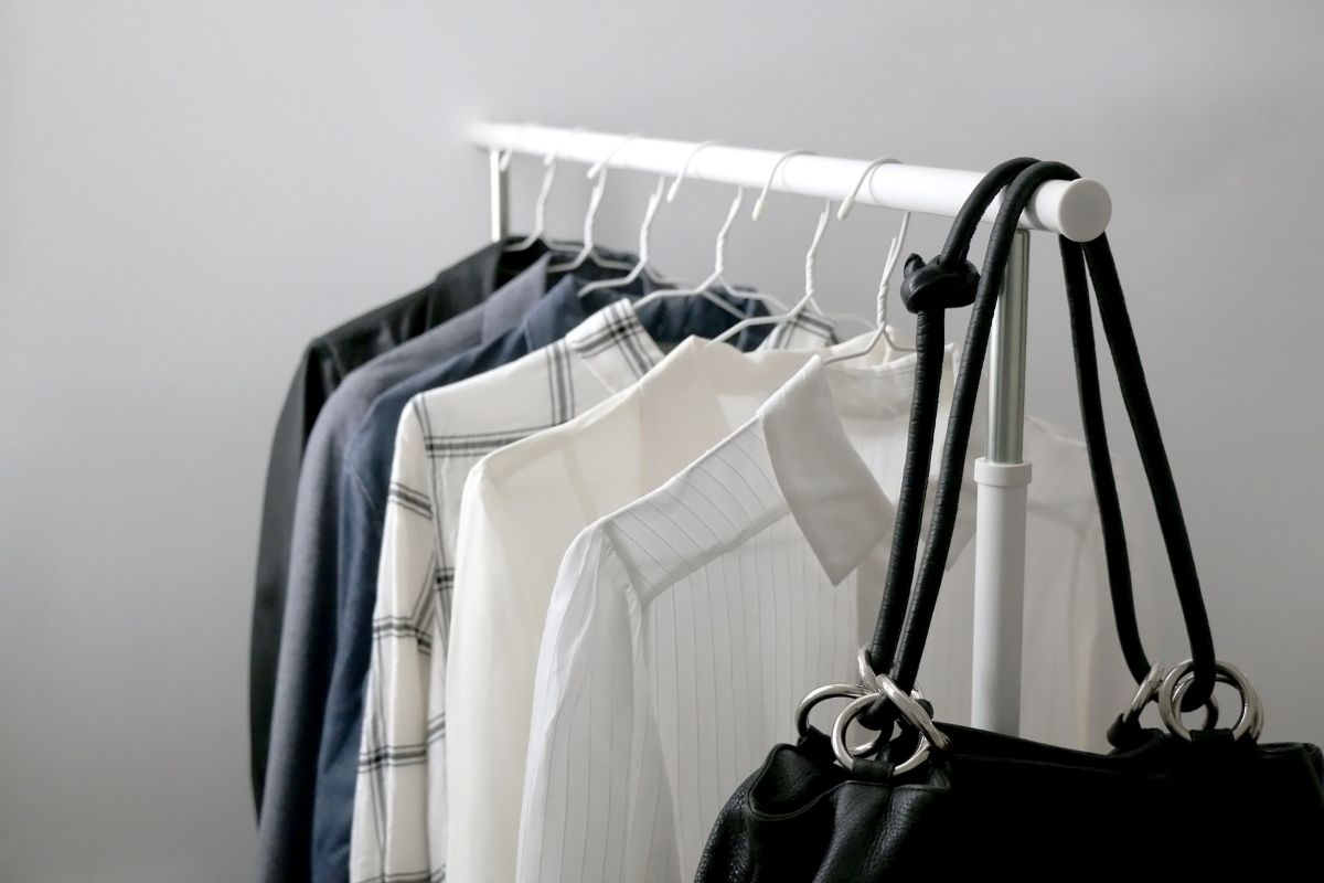 Clothing rack on wheels with six blouses hanging on it, and a black purse hanging on the end.