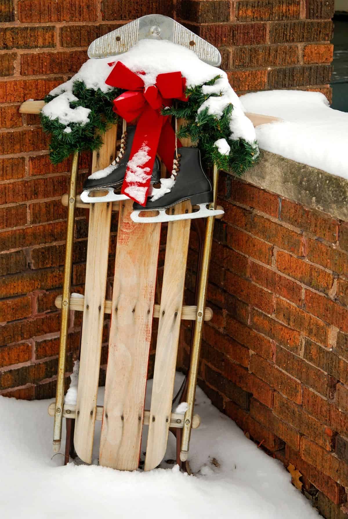 Wooden sled draped with ice skates leaning up against a brick wall