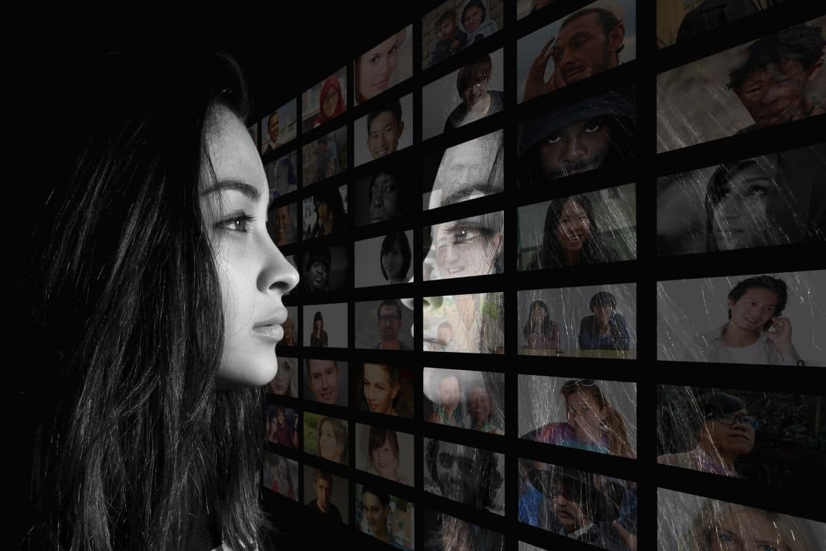 A woman on the left of the frame gazing into a grid of screens with different people. You can see her reflection on the grid of screens.