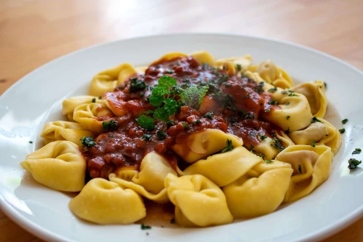Tortellini pasta on a white plate covered in meat sauce and garnished with fresh herbs.