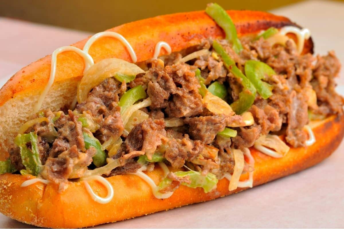 Closeup of a Philly Cheesesteak sandwich with a toasted hoagie roll, swirls of mayonnaise, and onions and peppers.