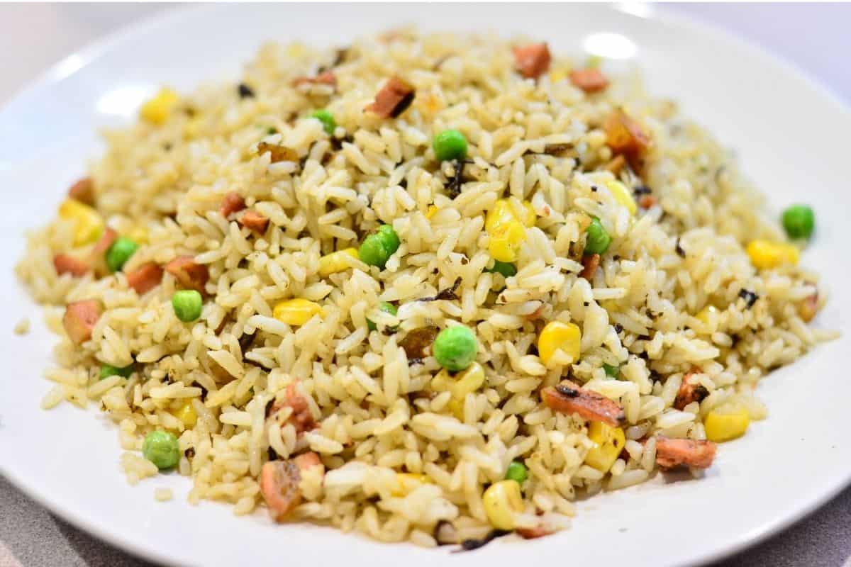 Closeup of a fried rice meal on a white plate. Includes peas, corn, pork, and egg pieces.