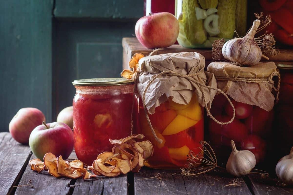 Four cans of fruits and vegetables surrounded by dried apples, garlic, and apples.