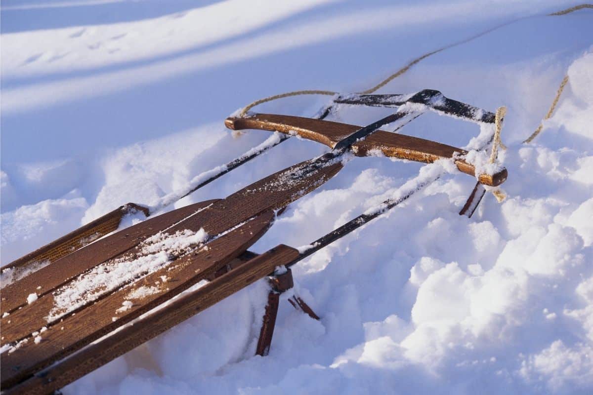 A wooden sled with metal runners sitting in a pile of snow.