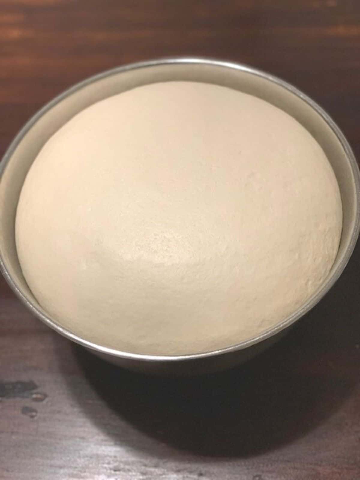 Risen bread dough in stainless steel bowl on a dark wooden tabletop