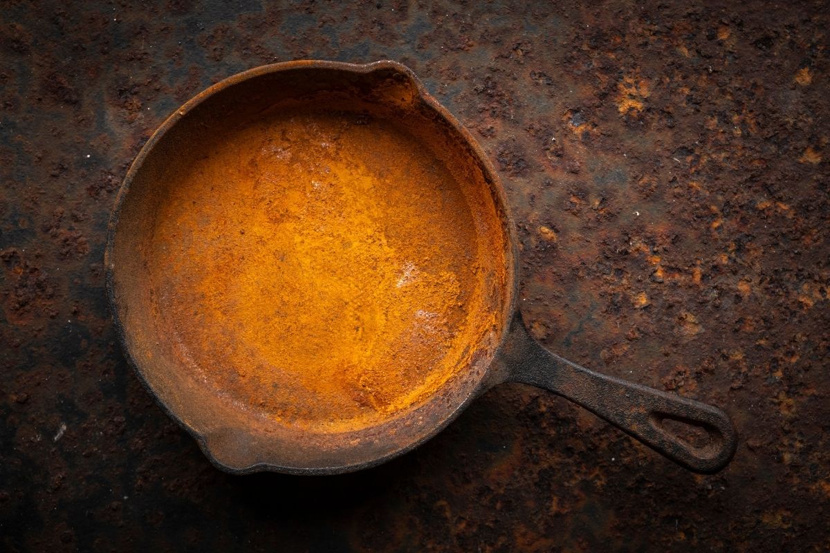 Cast Iron Skillet with bright orange rust all over it sitting on a rusted metal surface.