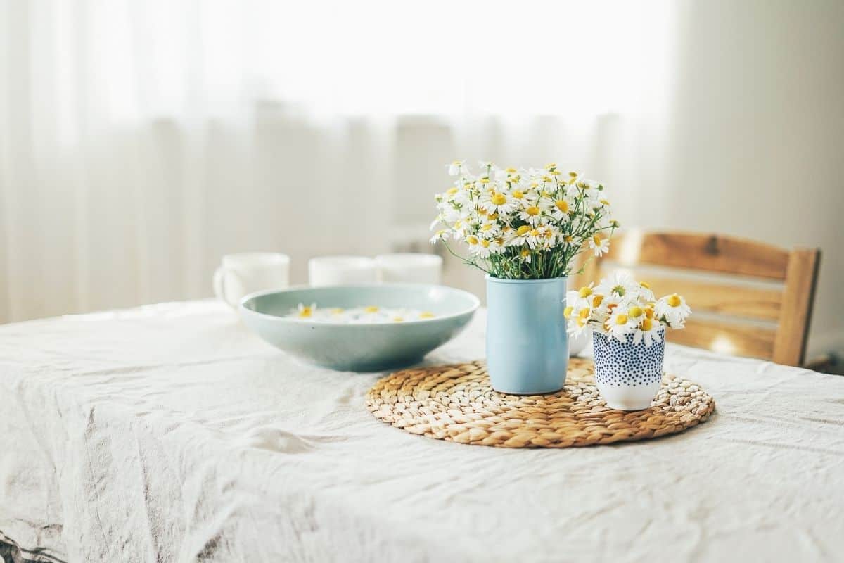 Table set with a white cloth with blue dishes filled with daisies.