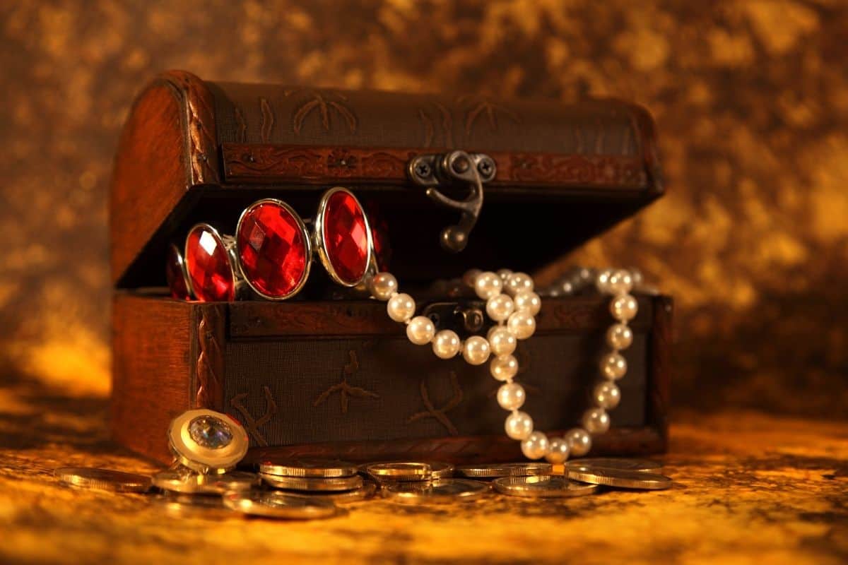 Treasure chest on a gold colored surface with a gold background. Chest is filled with gems and coins.