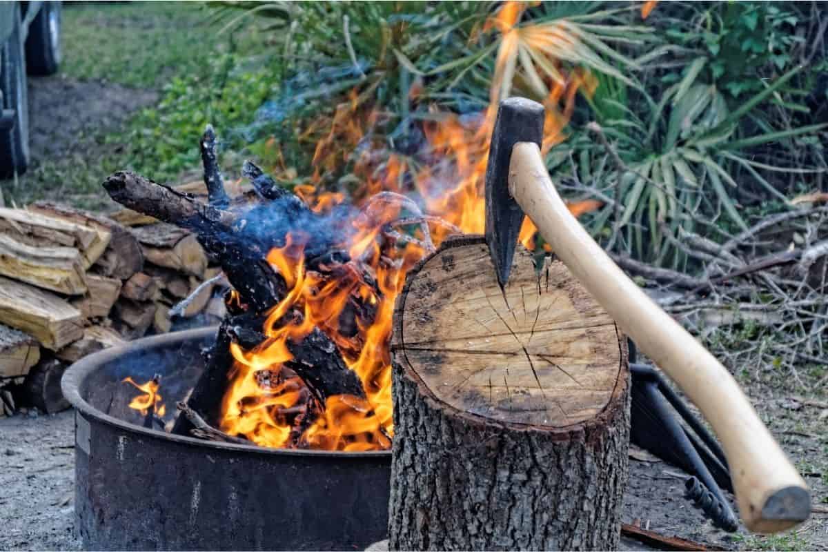 An axe is resting in a small piece of firewood with a fire in the background.