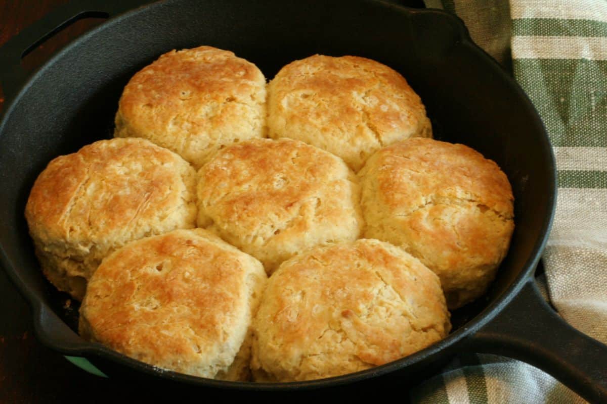 Cooked biscuits with golden brown top  in cast iron skillet resting on a linen tea towel.
