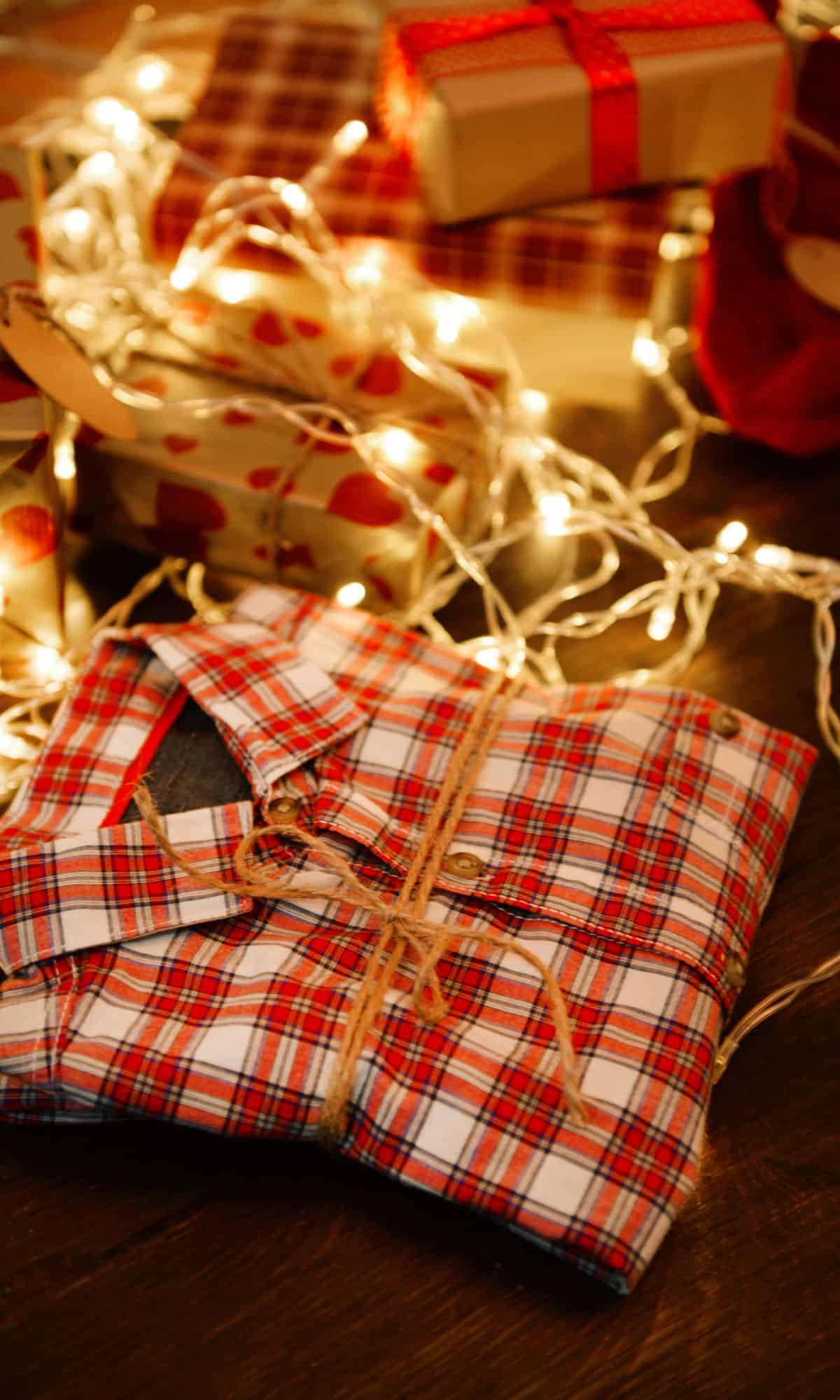 A pair of red plaid pajamas wrapped in twine under a Christmas tree surrounded by white Christmas lights