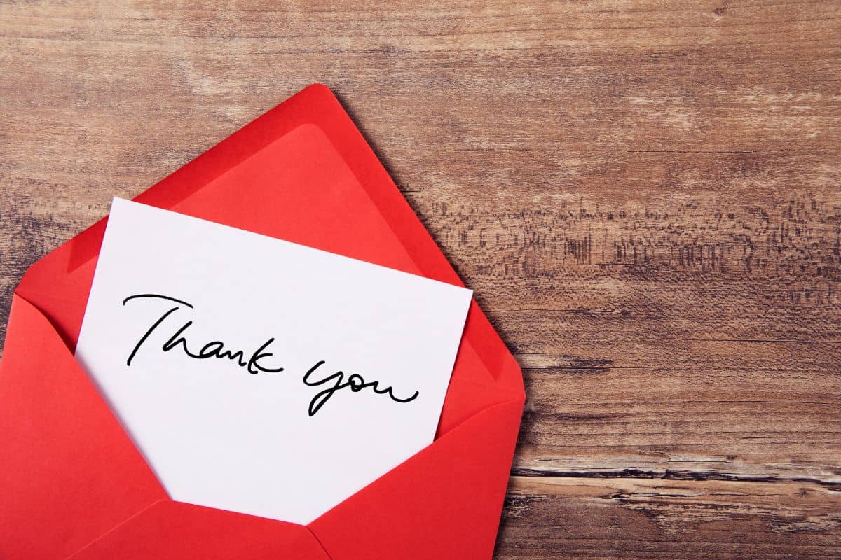 A red envelope with a black and white thank you card inside sitting on a rough wooden surface