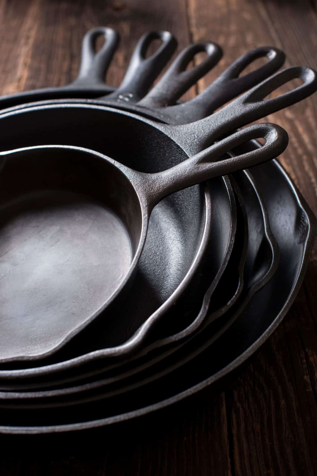 Stack of six cast iron skillets nested inside one another with their handles forming a swirl shape.
