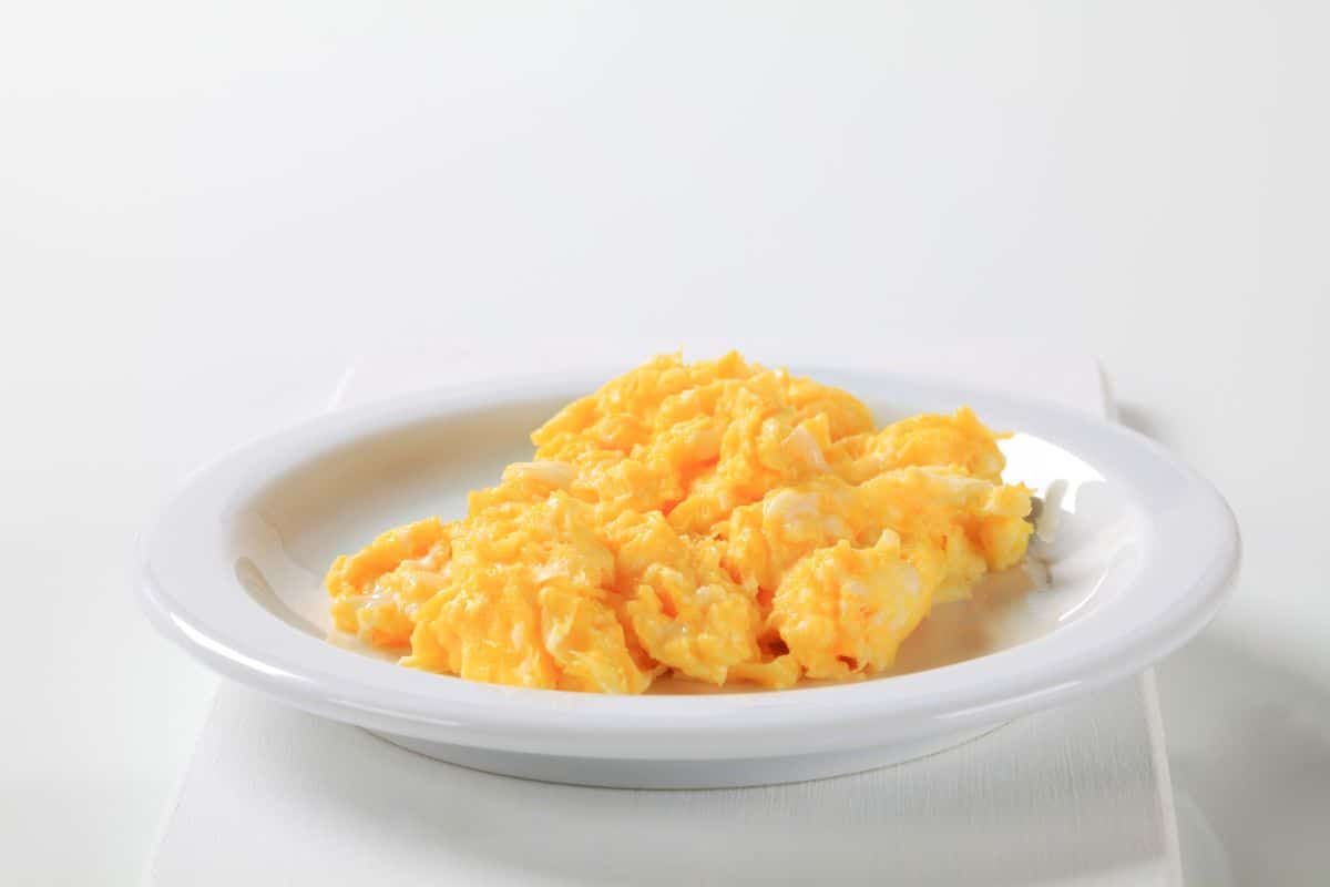 Minimalist Photo of Scrambled Eggs on a simple white plate on a simple white background.
